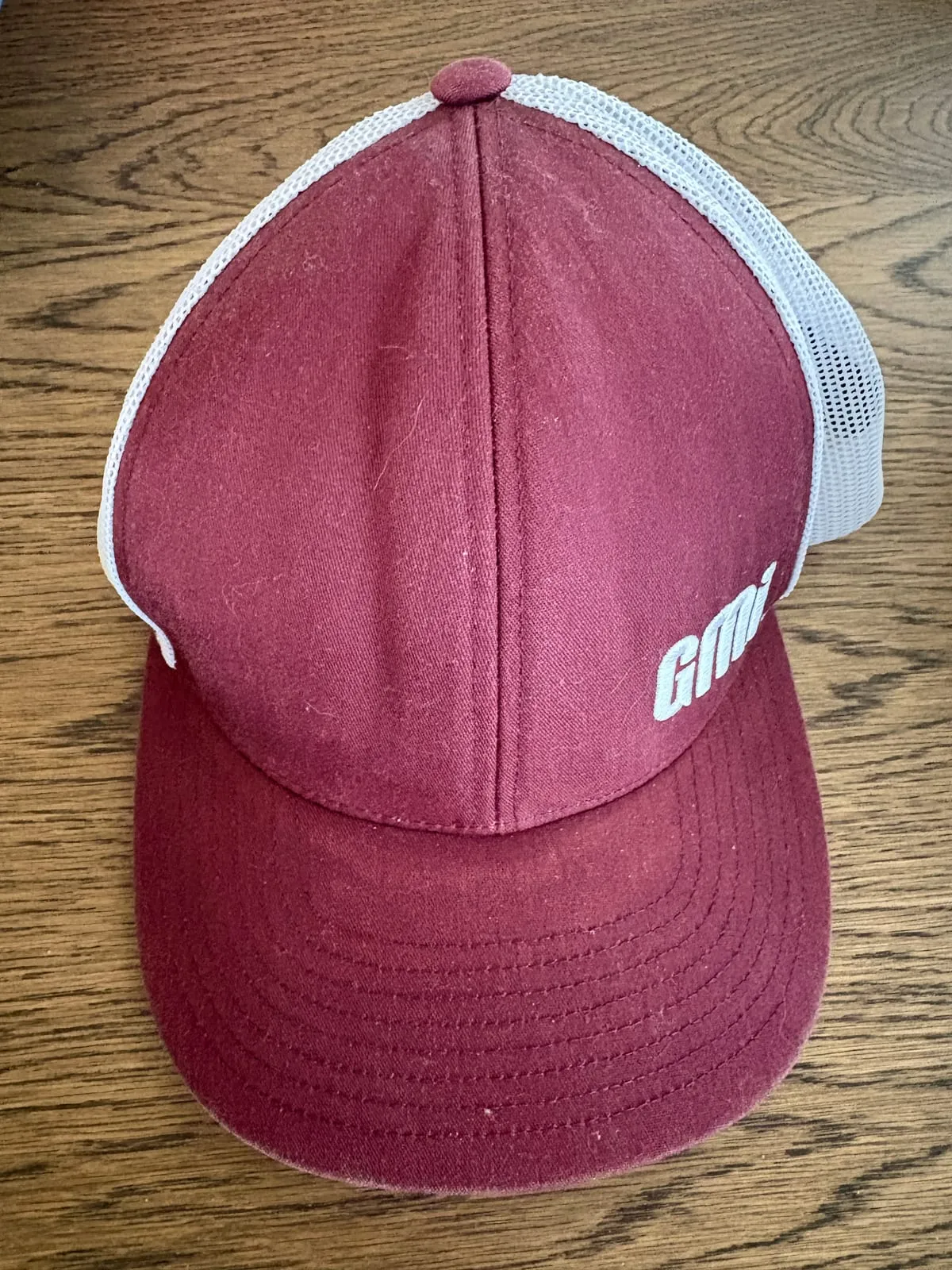 Retired maroon and white GMI trucker hat on a wood table
